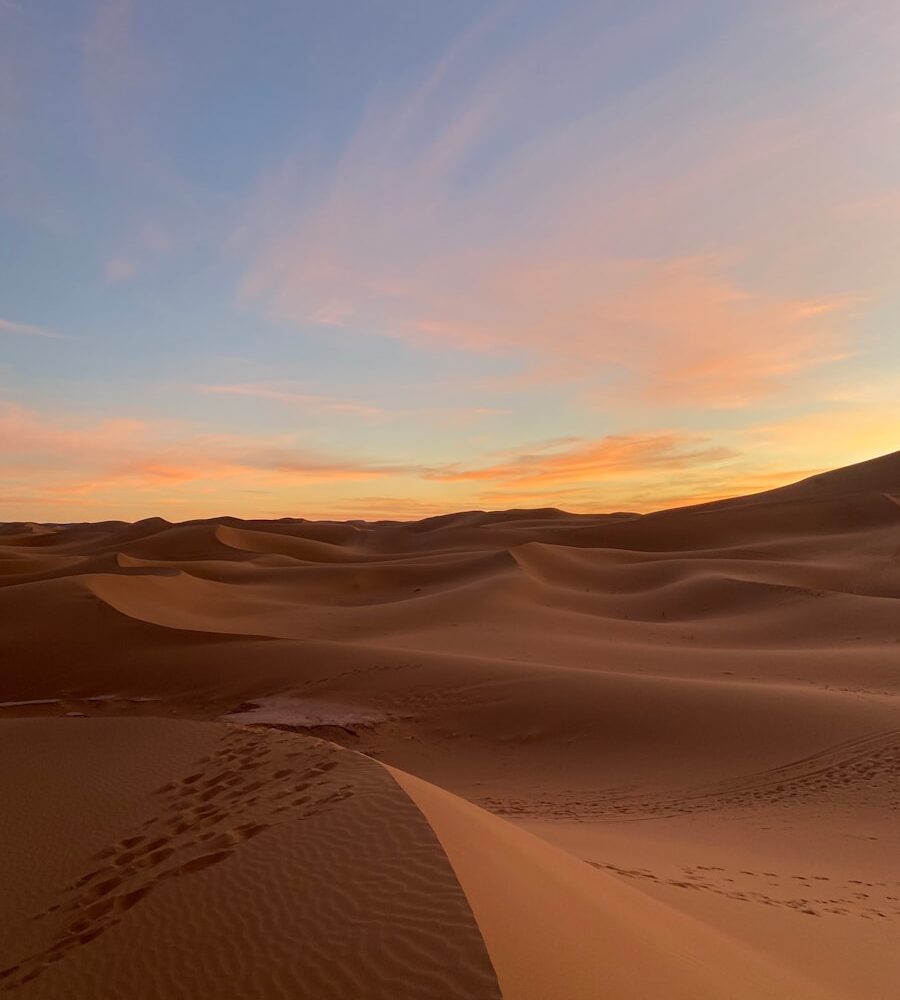 a sunset in the desert with footprints in the sand