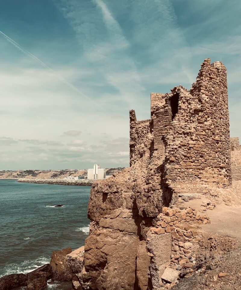 an old stone building sitting on top of a cliff next to the ocean