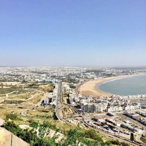 A stunning aerial view of an urban city with a sweeping coastline and busy roads, captured under a clear blue sky. Morocco itinerary 10 days From Agadir