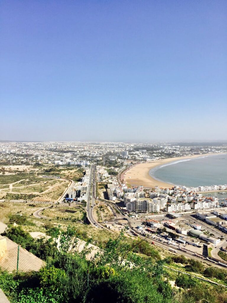 A stunning aerial view of an urban city with a sweeping coastline and busy roads, captured under a clear blue sky. Morocco itinerary 10 days From Agadir